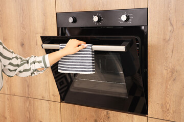 Woman opening modern oven in kitchen
