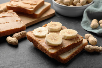 Fototapeta na wymiar Tasty peanut butter sandwiches with sliced banana and peanuts on dark gray table, closeup