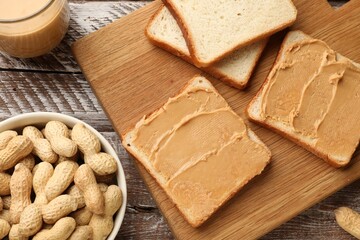 Tasty peanut butter sandwiches and peanuts on wooden table, flat lay