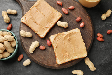 Tasty peanut butter sandwiches and peanuts on dark gray table, flat lay