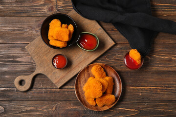 Plate and bowl of tasty nuggets and different sauces on wooden background