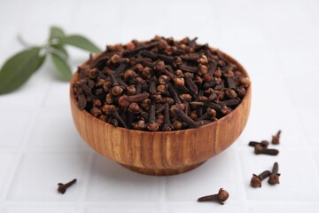 Aromatic cloves in bowl on white tiled table, closeup
