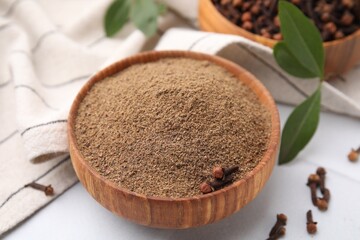 Aromatic clove powder and dried buds in bowl on white table, closeup