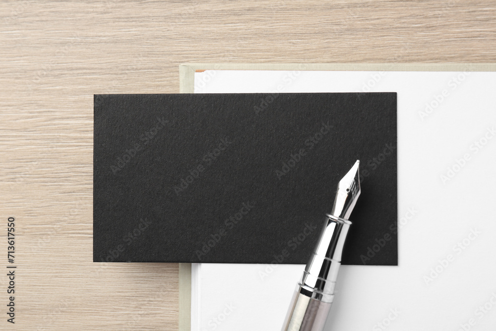 Wall mural Blank black business card, fountain pen and notebook on wooden table, top view. Mockup for design