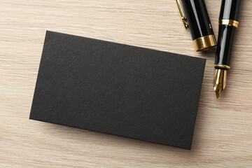 Blank black business card and fountain pen on wooden table, flat lay. Mockup for design