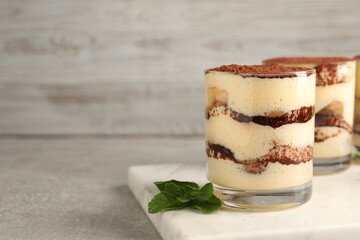 Delicious tiramisu in glasses and mint on grey textured table, closeup. Space for text