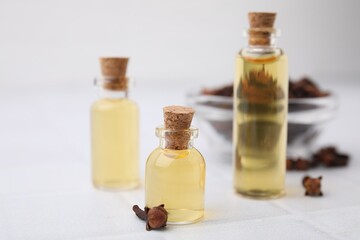 Clove oil in bottles and dried buds on white tiled table, closeup