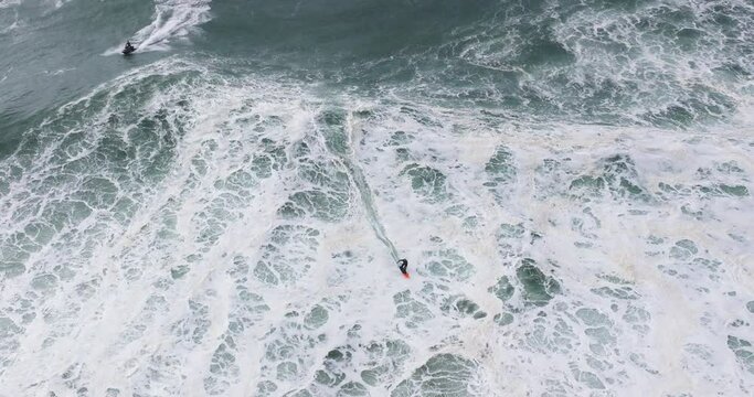 Aerial drone shot of big wave surfer surfing a big wave on a day with giant waves in Nazare, Portugal, Europe. Nazaré, big wave surfing town with biggest waves in the world. Shot in ProRes 422 HQ