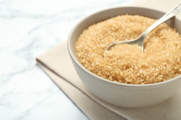 Brown sugar in bowl and spoon on white marble table, closeup. Space for text
