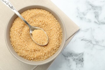 Brown sugar in bowl and spoon on white marble table, top view. Space for text