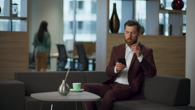Annoyed realtor throwing cellphone at sofa in modern corporate office interior.