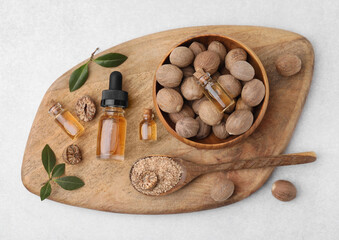 Nutmeg essential oil, nuts and leaves on light table, top view