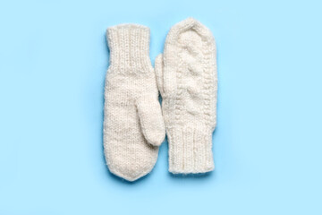 Pair of warm knitted mittens on blue background