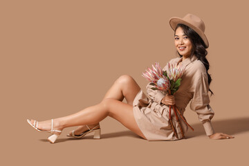 Young Asian woman with beautiful protea flowers sitting on brown background