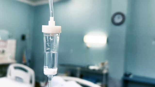 Drip chamber in an IV hangs on a medical infusion stand against the background of blurred medical beds in a clinic ward. Intravenous injections, medical care. Recovering patient in a hospital. Closeup