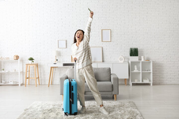 Happy young woman with suitcase and passport at home