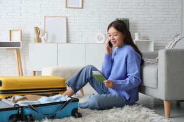 Young woman talking by mobile phone while sitting on floor near suitcases