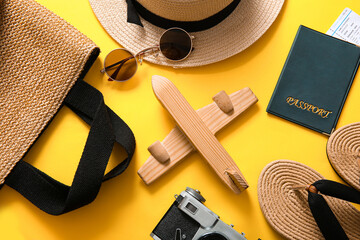 Composition with wooden plane, stylish beach accessories and passport on yellow background