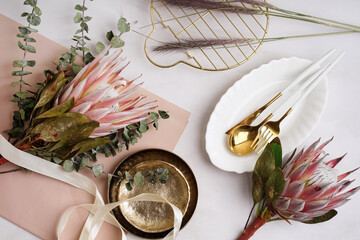 Composition with beautiful pink protea flowers, plates and cutlery on light background