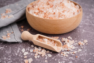 Wooden bowl and scoop with Himalayan pink salt on dark table