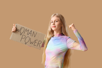 Young girl holding paper with text WOMAN POWER on beige background