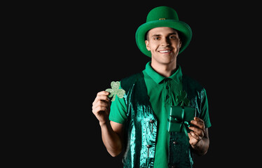 Happy young man with clover and gift on dark background. St. Patrick's Day