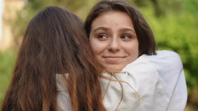 A beautiful girl hugged her friend standing in the outdoors. The girl smiles and looks at the camera. Close-up