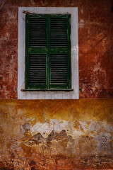 Imagen de una vieja ventana de una casa deshabitada con las paredes agrietadas.