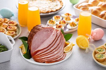 Easter brunch on large table with spiral sliced ham, quiche, deviled eggs and hot cross buns