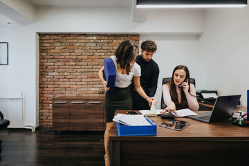 Focused business team analyzing documents in a modern office setting, with a woman on a phone call.