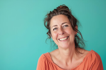 A woman in an orange shirt is smiling in front of a blue background