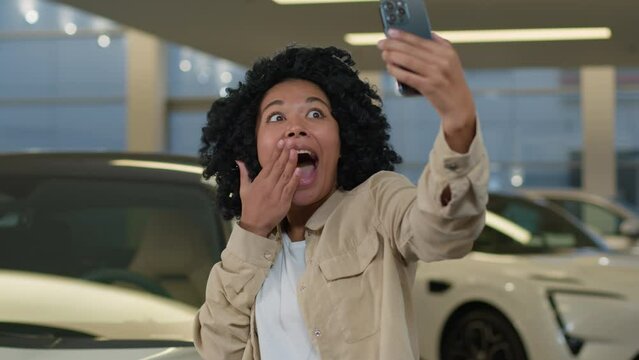 Joyful girl African American woman blogger taking selfie photo in car showroom buying new auto in dealership salon happy cheerful client buyer blogging with smartphone advertising automobile vehicle
