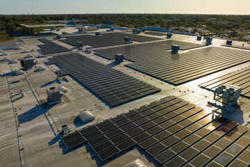 Fototapeta premium Aerial view of solar power plant with blue photovoltaic panels mounted on industrial building roof for producing green ecological electricity. Production of sustainable energy concept