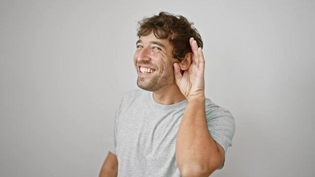 Deafness reality, happy young man in t-shirt cranking up his ear to listen over isolated white wall background, keen to hear and understand deaf rumor gossip