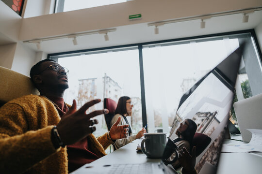 A young man in a mustard sweater engages with colleagues during a dynamic business meeting in a contemporary office setting, illustrating teamwork and collaboration.