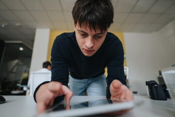 Handsome junior employee finds data online with his tablet.