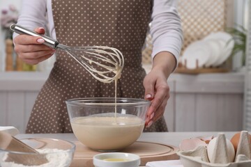 Woman making dough with whisk in bowl at table, closeup
