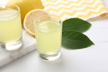 Tasty limoncello liqueur, lemons and green leaves on white table, closeup. Space for text