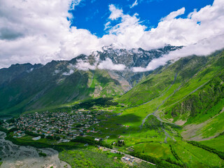 Fototapeta na wymiar Alpine village among green grassy mountains under the clouds - aerial photo.