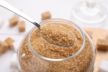 Taking brown sugar with spoon from jar, closeup