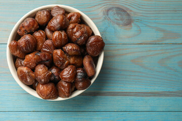 Roasted edible sweet chestnuts in bowl on light blue wooden table, top view. Space for text
