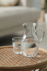 Jug and glass with clear water on wicker surface against blurred background