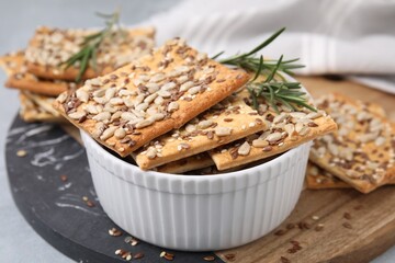 Cereal crackers with flax, sunflower, sesame seeds and rosemary in bowl on grey table, closeup