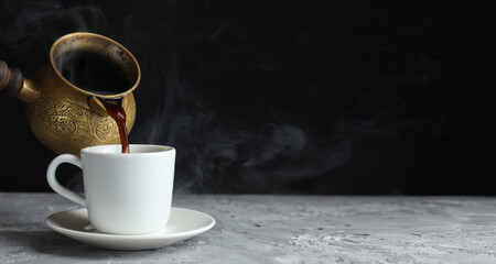 Turkish coffee. Pouring freshly brewed beverage from cezve into cup on grey table. Banner design with space for text