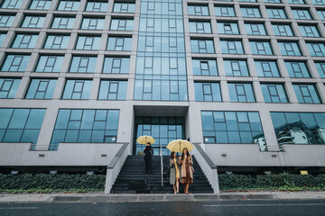 Two professionals carrying yellow umbrellas descending steps outside a contemporary urban office...