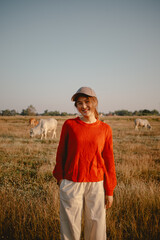 Happy asian woman in red sweater walking on the grass field to see the cows cattle and the sunset view.