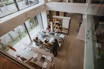 Overhead shot of a contemporary office setting with individuals focused on their work at desks, showcasing a collaborative workspace. - obrazy, fototapety, plakaty
