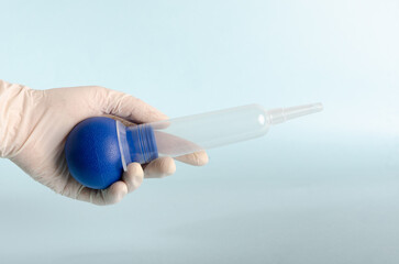 Bulb syringe, irrigation vacuum cleaner. Surgical instruments, isolated on light blue background, held by doctor's hand with white gloves. Closed angle. Copy space.