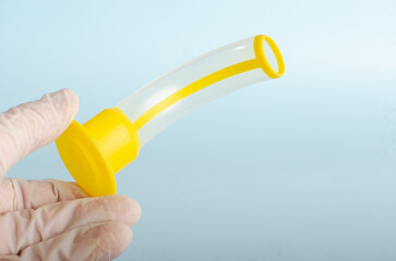 Guedel cannula. Orotracheal intubation, medical instruments, held in hand of doctor with white glove. Respiratory deficiency, first aid. Isolated on light blue background, closed angle.