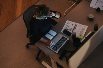 Above view of a focused businesswoman working at her desk with a laptop, documents, and coffee, in...